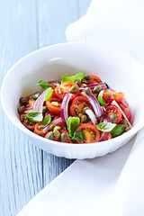 Simple salad with cherry tomatoes, red onion and fresh herbs. Bright wooden background. Close up.	