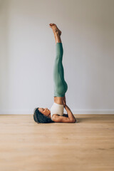 Young woman practicing supported shoulderstand yoga pose at home