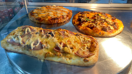 Freshly baked mozzarella pizza displayed at display case with warm lighting inviting a delicious culinary experience. Pizza Showcase