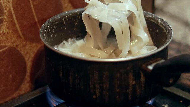 Flat rice noodles known as Kuey Teow, Kuay Tiew, or Hor Fun boiling in a pot on a stove in preparation for cooking stir-fry dish