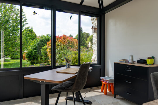 V&eacute;randa moderne lumineuse avec baies vitr&eacute;es et mobilier contemporain, ouverte sur un jardin verdoyant.