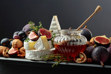 Camembert cheese with fruits and honey on a black background.