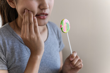 Woman suffering tooth pain from eating candy. Concept of tooth sensitivity, dental cavity, oral health problem, sugar damage, and unhealthy eating habits.