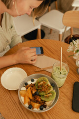 Middle-aged woman scrolls her social media feed on mobile phone in a cozy cafe. Small business. Using phone for business, online shopping, transfer money, financial, internet banking