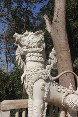 Decorative White Singha at Temple Entrance. Side view of a white Singha guardian statue with elaborate carvings, located at the gate of a Thai temple under bright sunlight.