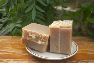 Handmade Tamarind Oatmeal Soap Bars. A stack of handmade tamarind and oatmeal soap bars placed on a white dish, photographed outdoors in natural lighting with a green garden background. 