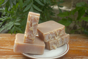 Handmade Tamarind Oatmeal Soap Bars. A stack of handmade tamarind and oatmeal soap bars placed on a white dish, photographed outdoors in natural lighting with a green garden background.
