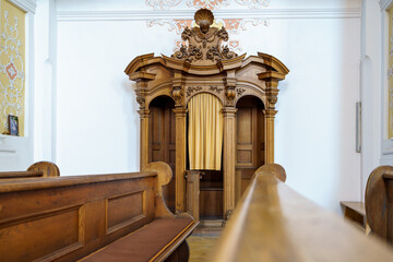 Traditional wooden confessional in a serene church setting with simple decor and historical...