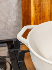 A white pot on a stove with a wooden cutting board behind it