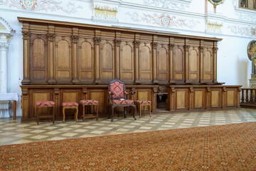 Elegant wooden benches and chairs inside a historic church hall with intricate decor and patterned...
