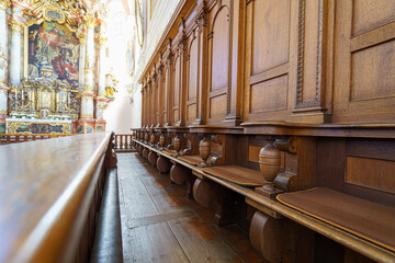 Historic wooden benches line the walls of a beautifully ornate church with a detailed altar in the...