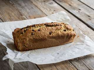 freshly baked banana bread on baking paper on a rustic wooden table. Side natural light.