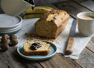 Ceramic jug serving chocolate on a slice of homemade banana bread, accompanied by coffee, fruit and nuts. Slow and conscious living, artisanal breakfast.