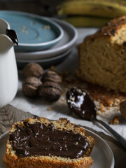 Artisanal and slow breakfast on a wooden table with natural side light. Banana bread with chocolate, impregnated peas, cup of coffee, fresh fruit and nuts. Natural and welcoming layout