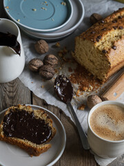 Artisanal and slow breakfast on a wooden table with natural side light. Banana bread with chocolate, impregnated peas, cup of coffee, fresh fruit and nuts. Natural and welcoming layout