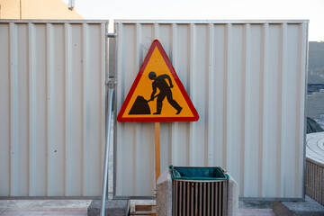 men at work caution sign at ongoing construction site in urban area