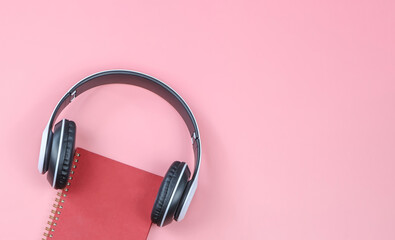 flat lay of red  diary or planner covered with headphones on pink background with copy space.