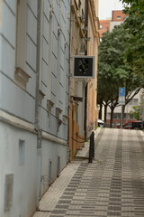 The scene shows a narrow street with unique buildings, a tidy sidewalk, clear signs, and lush...