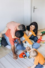 Happy parents sitting on the floor with their three sons, laughing, tickling each other, and...