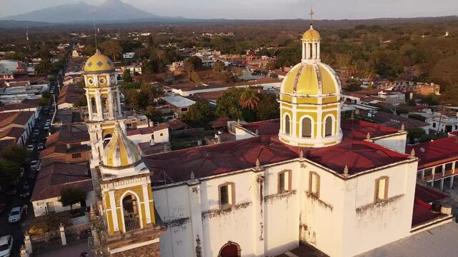 Drone view of San Miguel Arcangel church surrounded by red-roofed buildings and mountains at sunset