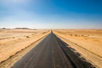 Endless Desert Road Stretching into Horizon Under Clear Blue Sky, Capturing Solitude and Vastness of Arid Landscape in Warm, Sunny Conditions