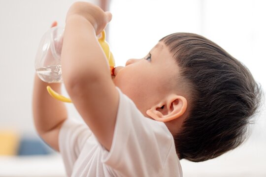 Young child drinks from a colorful sippy cup indoors during the daytime
