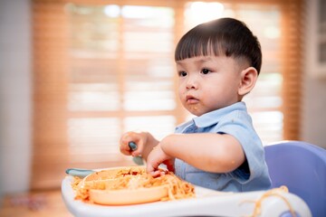 Young child enjoying a meal of spaghetti in a bright kitchen while sitting in a high chair