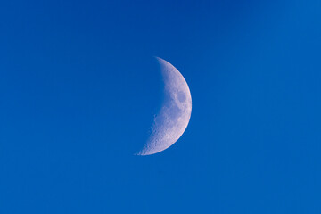 Waxing gibbous moon in a deep blue evening sky. Detailed surface texture captured through a telescope. Peaceful and minimalist night sky astronomy scene.
