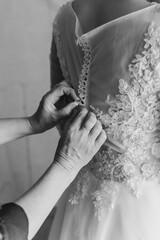 Close-up of the bride's mother's hands fastening the buttons on her dress