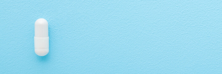 White capsule pill on light blue table background. Pastel color. Closeup. Wide banner. Empty place for text. Top down view.