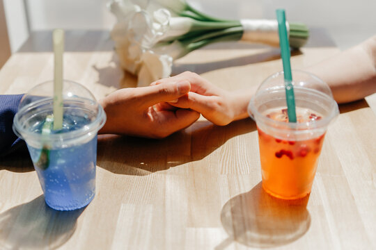 Two cups of different colored drinks on a table. One is blue and the other is red. A hand is touching another hand