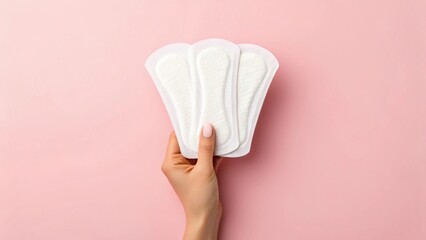 Hand holding multiple sanitary pads against a pink background, emphasizing feminine hygiene products.
