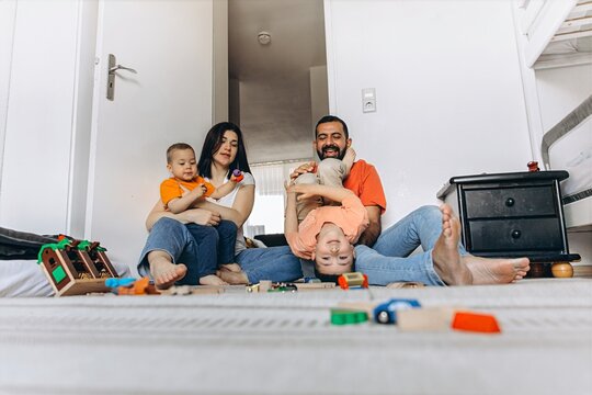 Mom and dad tickle and play with their children on the floor in a colorful playroom. They laugh, bond, and share joyful, loving moments of family fun and connection