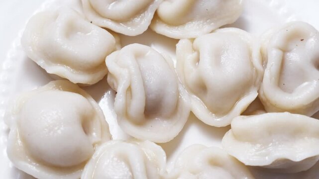 revolves. Boiled dumplings and cream are arranged in a circle on a white plate. The plate with dumplings is set against a light background, creating a simple and appetizing composition.