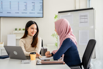 Multiracial young female employees work on laptop discuss business cooperation ideas at meeting...
