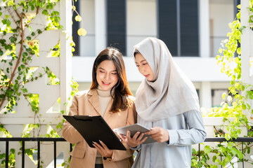 Muslim businesswoman wearing hijab holding tablet and talking with female colleague who's holding...