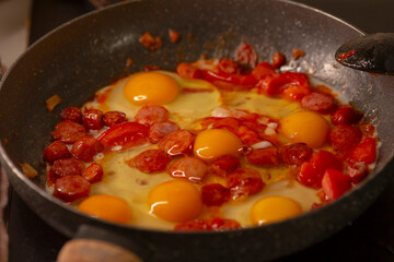 A pan is filled with delicious sausages that are sizzling and cooking beautifully alongside fresh eggs in a heated skillet placed on a stovetop, creating a mouthwatering meal for breakfast