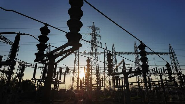 Silhouettes of electrical parts and structural elements of a power plant at sunset. the sun appears and disappears through the structure due to the movement of the camera.