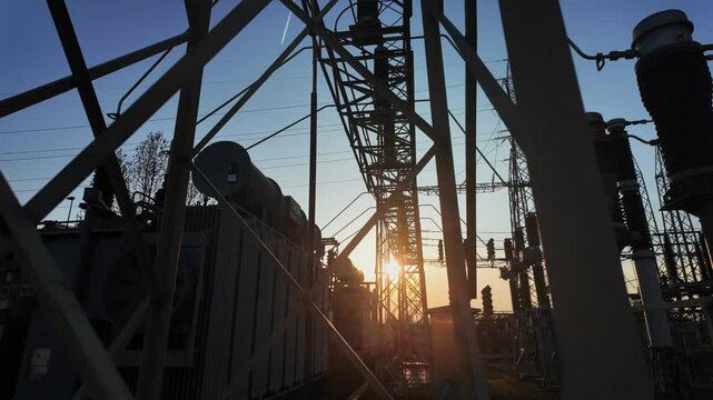 Silhouettes of electrical parts and structural elements of a power station at sunset. the sun appears and disappears through the structure due to the movement of the camera.