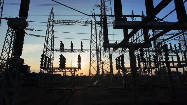 Silhouettes of electrical parts and structural elements of a power plant at sunset. the sun appears and disappears through the structure due to the movement of the camera.