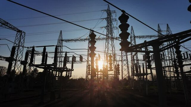 Silhouettes of electrical parts and structural elements of a power station at sunset. the sun appears and disappears through the structure due to the movement of the camera.
