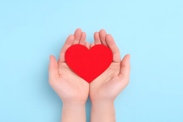 Fototapeta premium Hands Holding a Paper Red Heart Shape Top view Isolated On Blue Backdrop