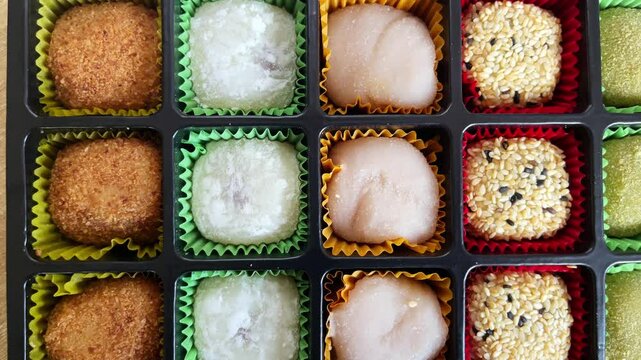 Colorful assortment of mochi desserts arranged in decorative box, showcasing various flavors and textures.Traditional Japanese rice sweet with soft, chewy texture.