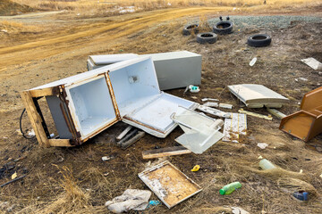 Broken fridge lies discarded on a muddy roadside, refrigerator with rusted doors open. Scattered debris surround the wrecked appliance, pollution and neglect. Environmental damage after a disaster.