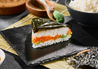 Salmon onigiri on dark stone plate, bright natural lighting, minimalist Japanese food composition