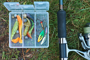 Fishing tackle on the grass near the river. Spinning rod and box with wobblers, spinners. Selective focus