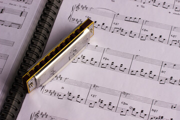 Fototapeta premium A metal harmonica on an open music book. taken in close-up, with space for text, an object, or an advertisement