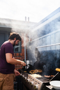Man cooking potato chips on backyard barbecue in sunlight