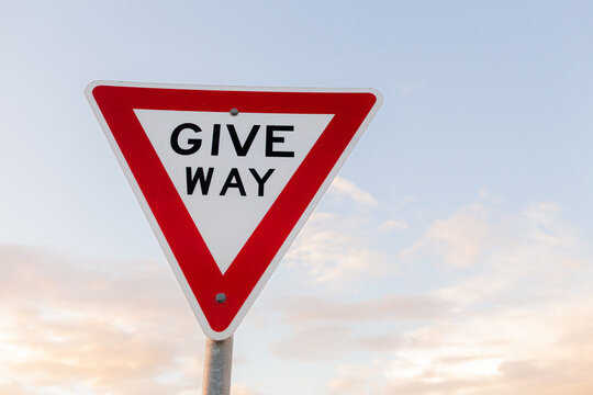 Give way sign on post with soft pastel sky backdrop at dusk