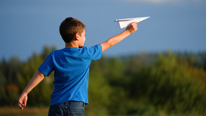 Plakat A child in a blue shirt holds a paper airplane outdoors.